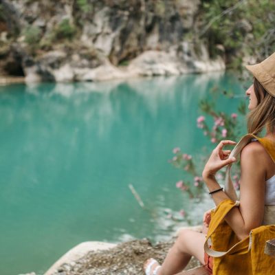 Woman in Beige Bucket Hat Sitting on a Bench on a Mountain Lake Shore
