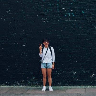 Woman in Blue Denim Shorts Standing in Front of Black Brick Wall