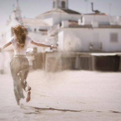 Woman Running on Sand Near White Concrete Building